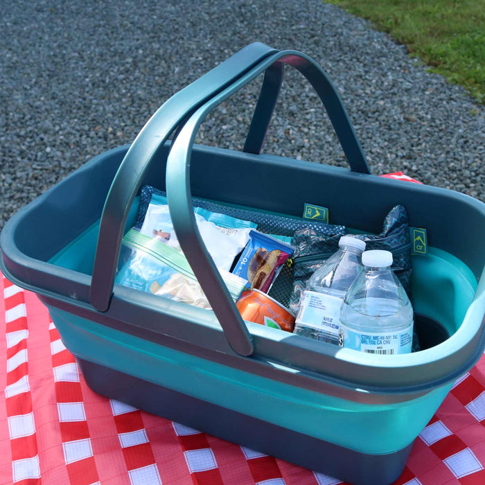 The Adventure Ready Picnic Basket shown on a picnic table holding drinks, food, and the Bamboo Dining Set inside.