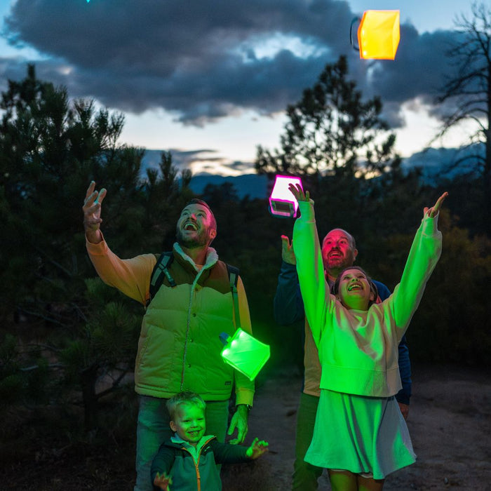 A smiling family throwing colorful lanterns in the air at a campsite